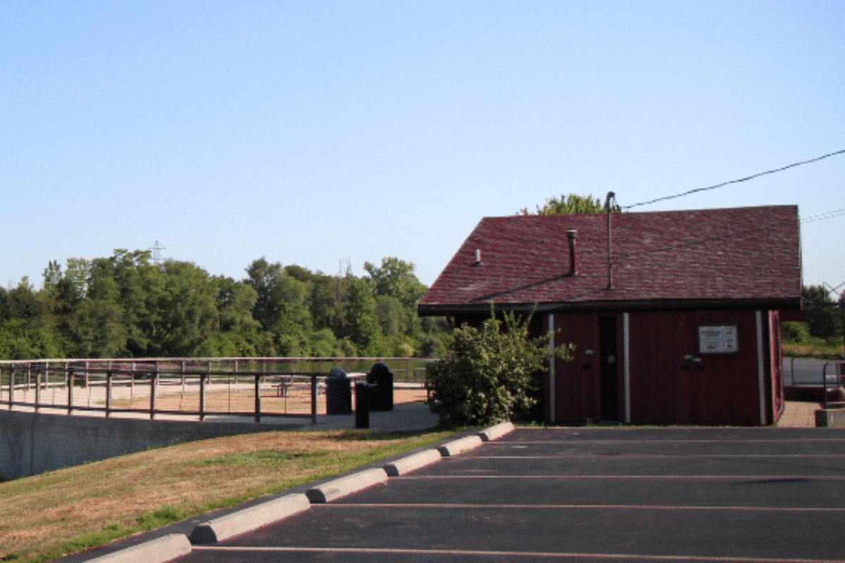 Red wooden concession-style building with a sloped roof beside a paved parking lot under a clear blue sky.