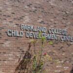 Brick wall with the sign 'Parkland College Child Development Center' on a brick building, with a small flowering shrub in front.