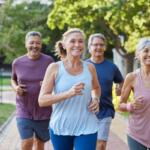 Four adults jogging together on a sunlit park path, smiling as they run.