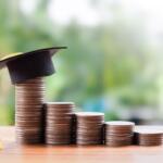 Stacks of coins in increasing height on a wooden surface, topped with a graduation cap and yellow tassel, symbolizing education savings or success