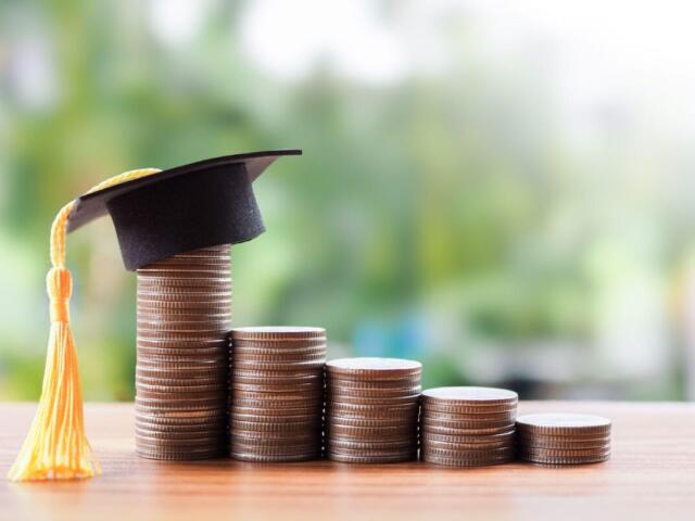 Stacks of coins in increasing height on a wooden surface, topped with a graduation cap and yellow tassel, symbolizing education savings or success