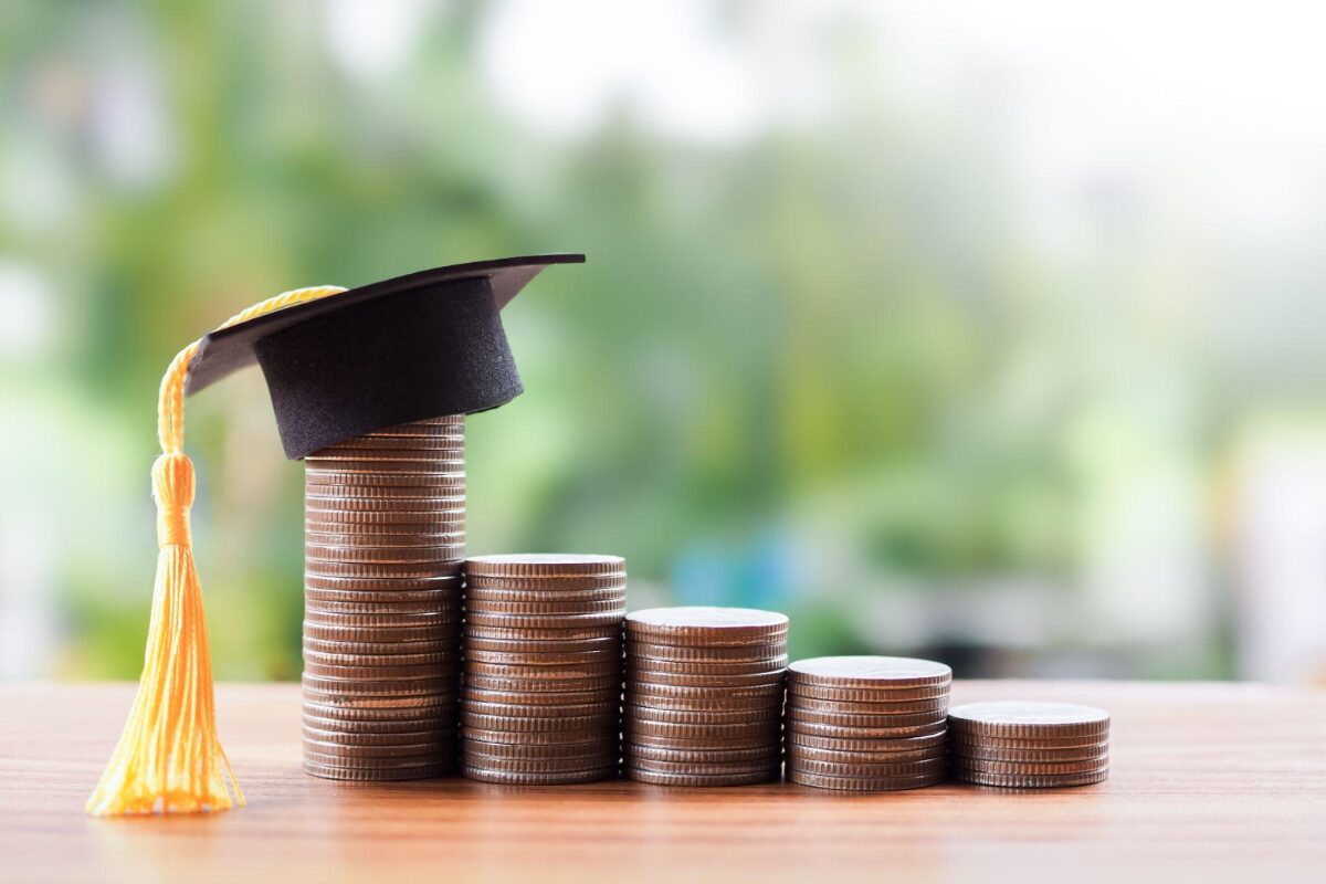 Stacks of coins in increasing height on a wooden surface, topped with a graduation cap and yellow tassel, symbolizing education savings or success