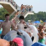 Group of kids and adults in inflatable inner tubes at a crowded outdoor water park, with a tall viewing platform in the background.