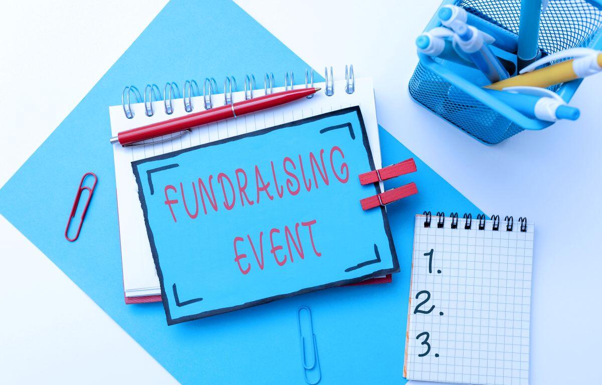 Blue sign reading 'Fundraising Event' placed on a desk with notebooks and office supplies.