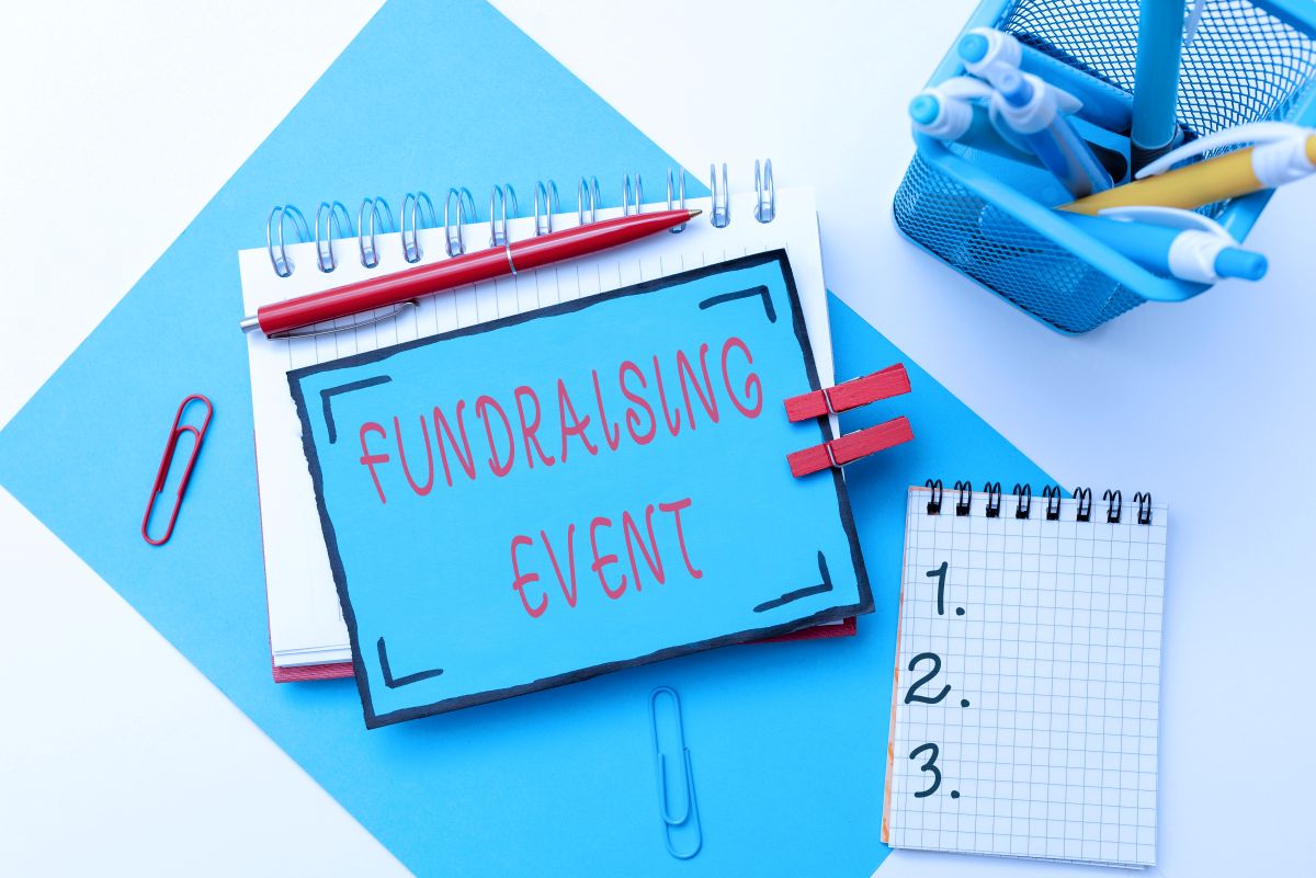 Blue sign reading 'Fundraising Event' placed on a desk with notebooks and office supplies.