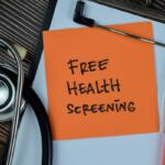 Orange note on a clipboard reads 'Free Health Screening' beside a stethoscope and a pink liquid sample tube nearby.