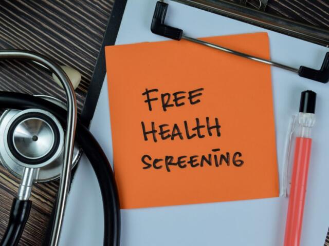 Orange note on a clipboard reads 'Free Health Screening' beside a stethoscope and a pink liquid sample tube nearby.