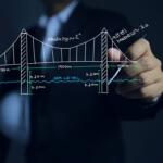 Person in a suit draws a suspension-bridge sketch with measurements (700 m, 1500 m) and sea level line on a transparent board/textbook-style diagram
