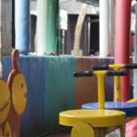 Colorful outdoor playground equipment with yellow see-saw seats and handlebars among red, blue, and green posts.