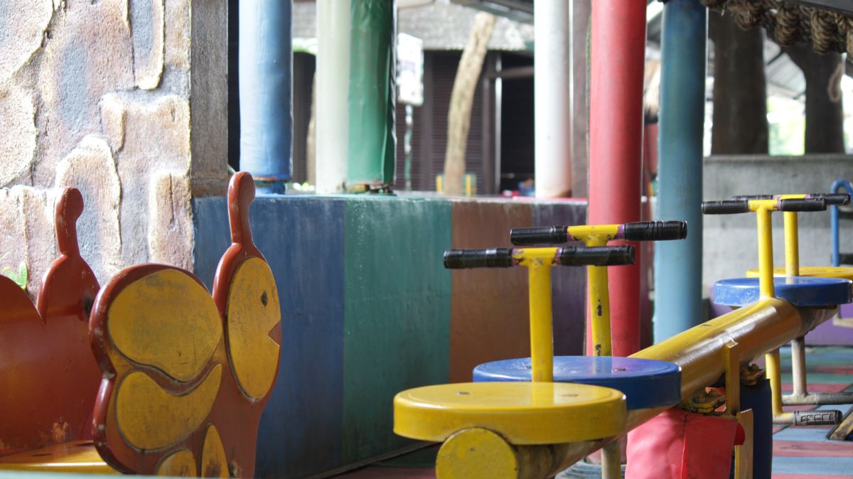 Colorful outdoor playground equipment with yellow see-saw seats and handlebars among red, blue, and green posts.