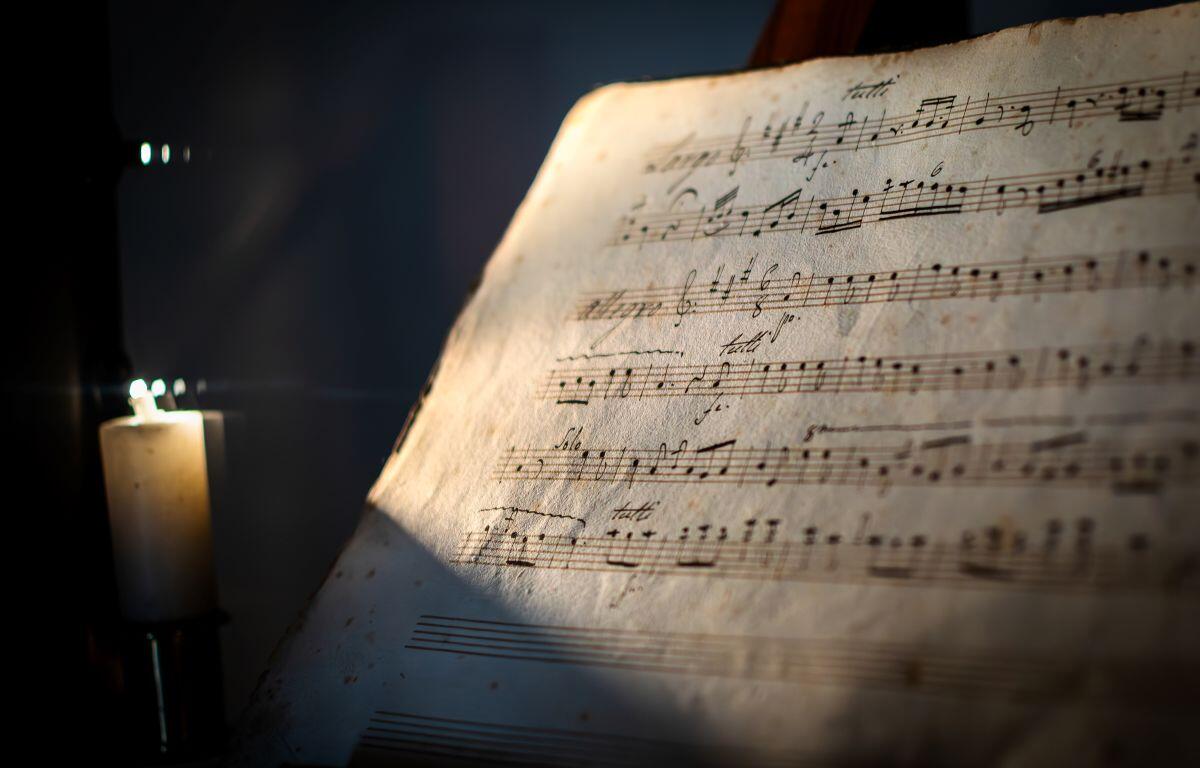 Old, worn sheet music on a stand lit by a candle, warm glow highlighting the musical notes.
