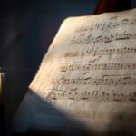 Old, worn sheet music on a stand lit by a candle, warm glow highlighting the musical notes.
