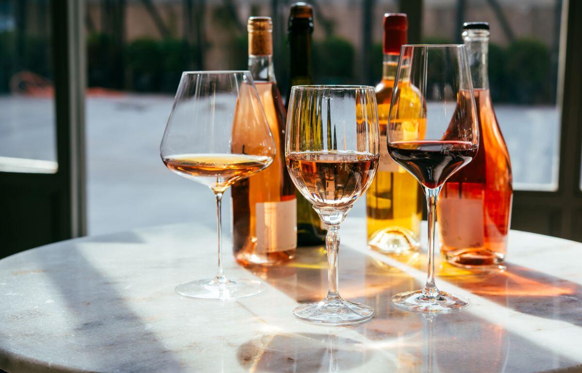 Three wine glasses on a marble table with assorted bottles in the background.