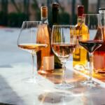 Three wine glasses on a marble table with assorted bottles in the background.