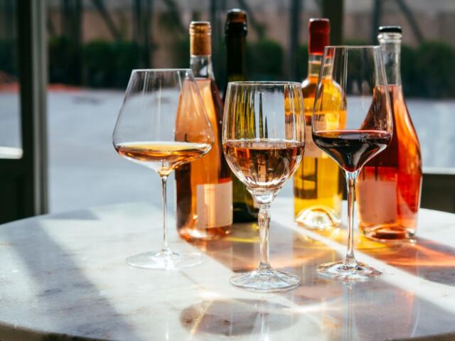 Three wine glasses on a marble table with assorted bottles in the background.