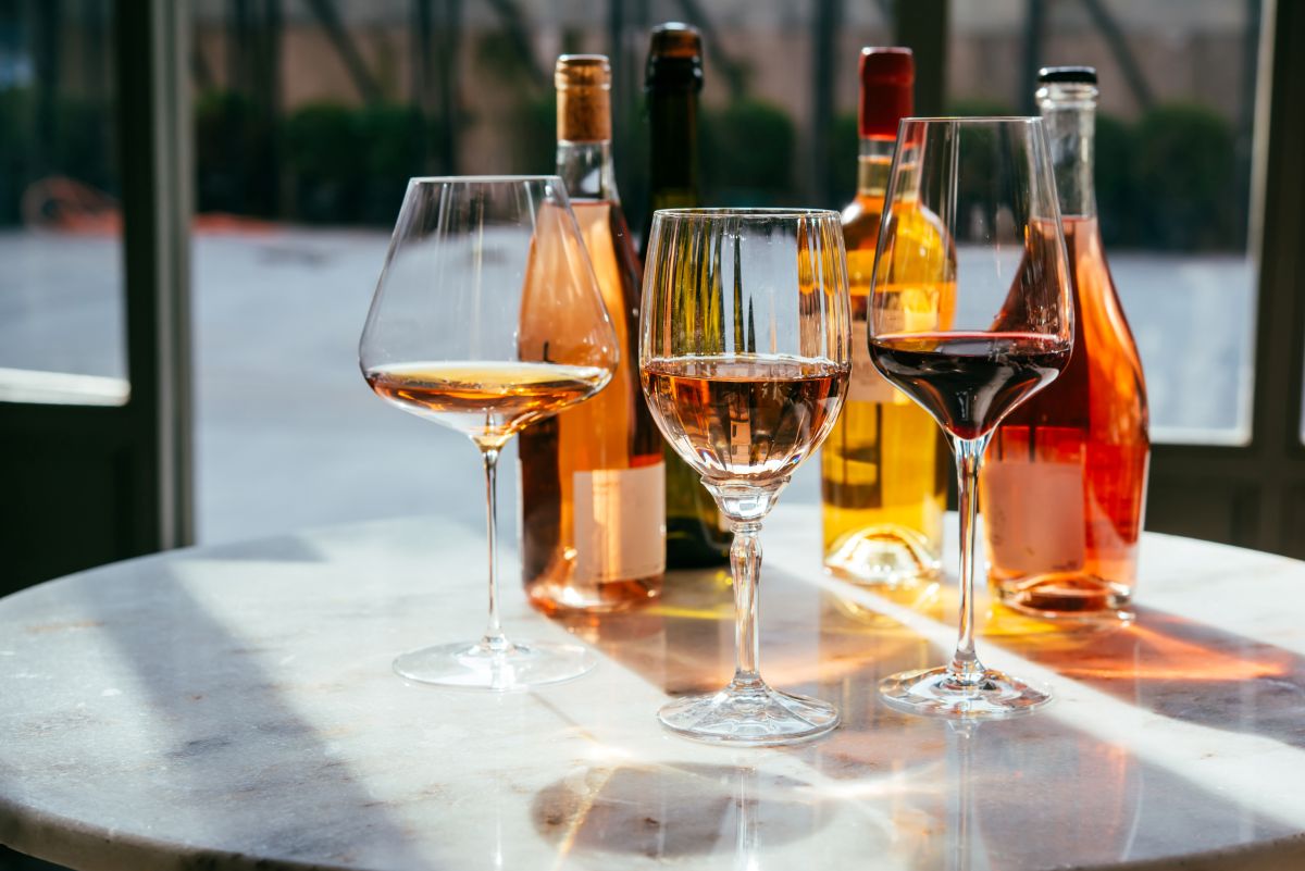 Three wine glasses on a marble table with assorted bottles in the background.