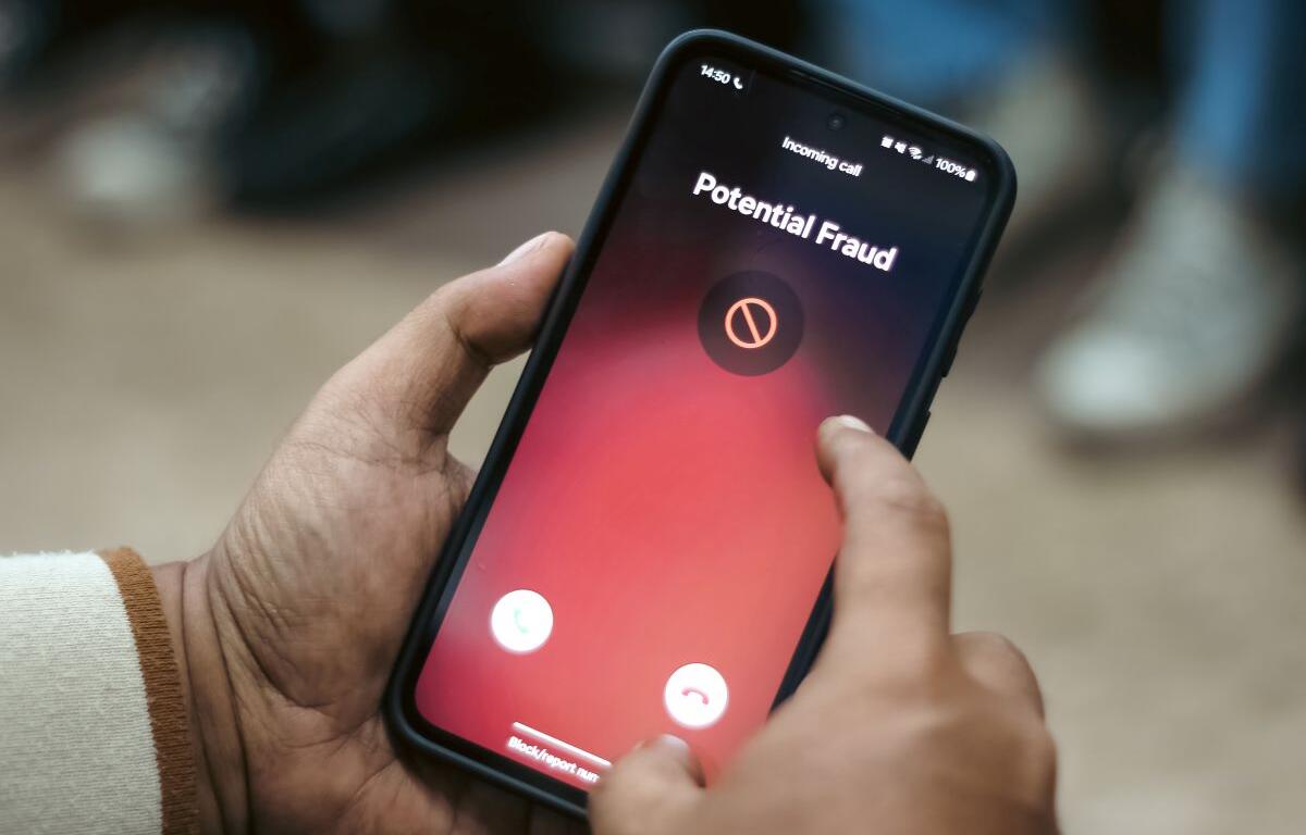 Smartphone screen showing an incoming call warning: 'Potential Fraud' on a red gradient background, held in a person's hands as they swipe.
