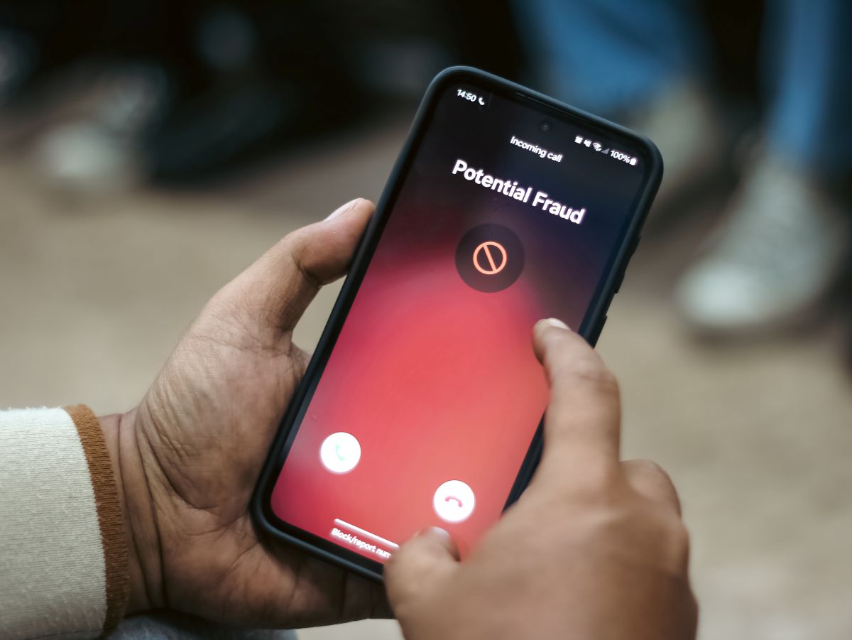 Smartphone screen showing an incoming call warning: 'Potential Fraud' on a red gradient background, held in a person's hands as they swipe.