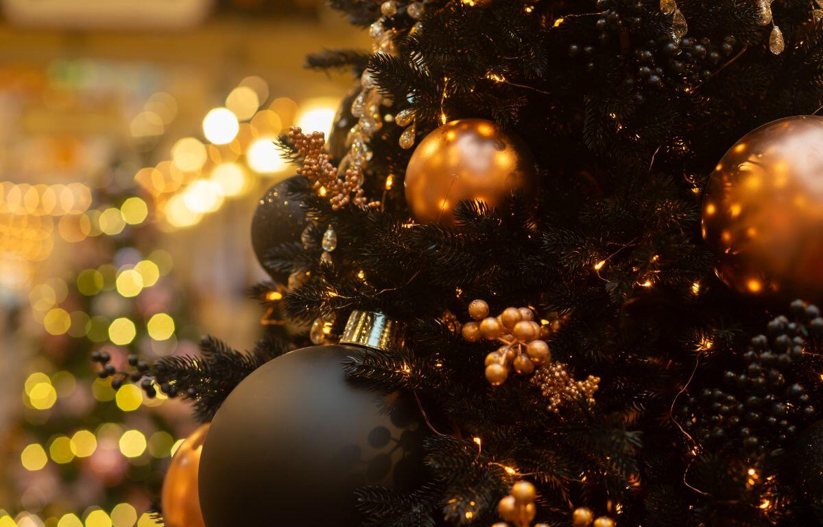 Close-up of a Christmas tree decorated with gold and black baubles, berries, and warm fairy lights