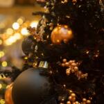 Close-up of a Christmas tree decorated with gold and black baubles, berries, and warm fairy lights