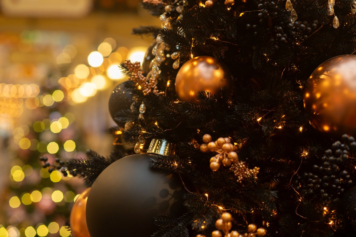 Close-up of a Christmas tree decorated with gold and black baubles, berries, and warm fairy lights