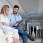 Doctor and patient sit on a hospital bed as the doctor reviews a tablet, with blue holographic medical circuit graphics overlaying the scene.