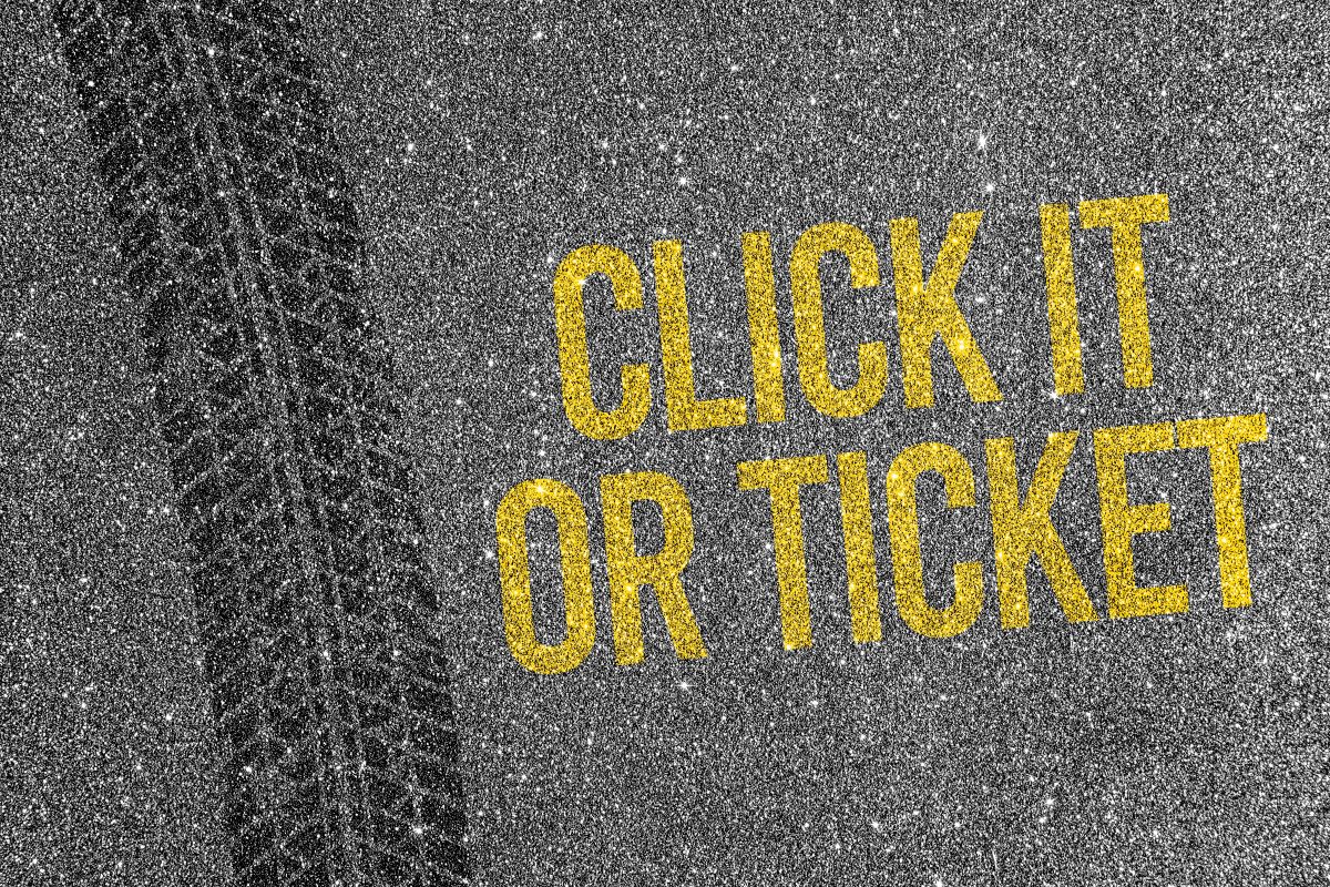 Yellow stenciled message 'CLICK IT OR TICKET' on an asphalt road beside a tire track.