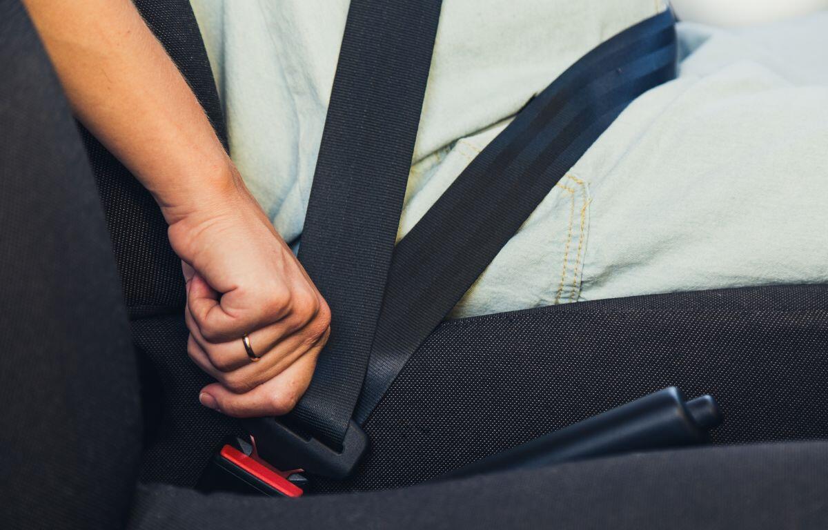 Person fastening a seatbelt in a car, hand near the red buckle.
