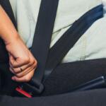 Person fastening a seatbelt in a car, hand near the red buckle.