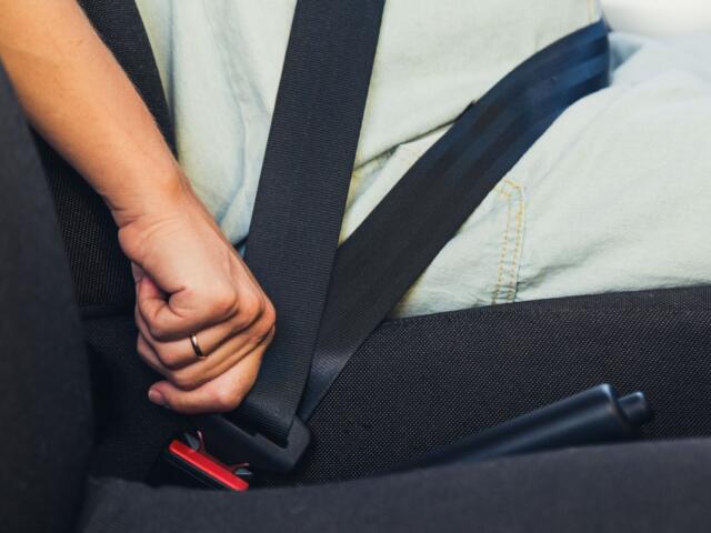 Person fastening a seatbelt in a car, hand near the red buckle.