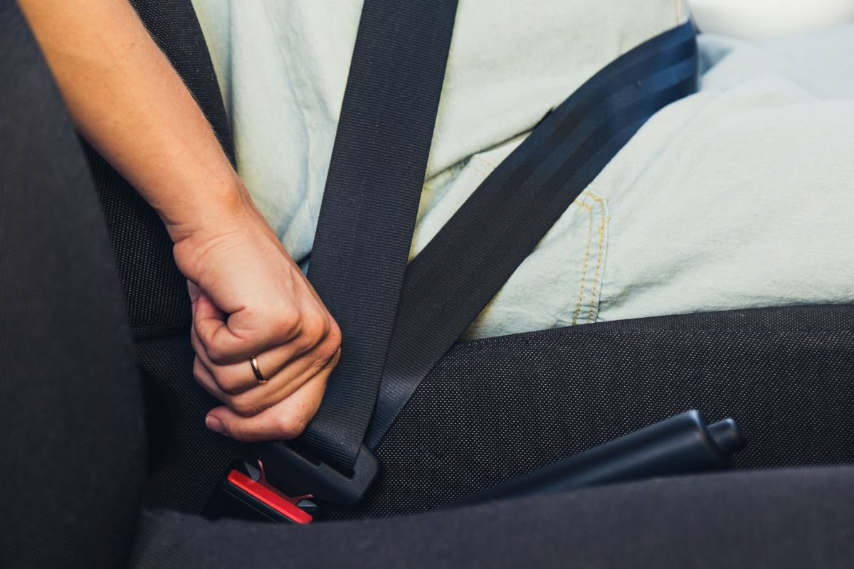 Person fastening a seatbelt in a car, hand near the red buckle.