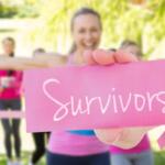 Group of women in pink exercise outfits holding a pink card that says 'Survivors' at a park, pink ribbon visible for breast cancer awareness