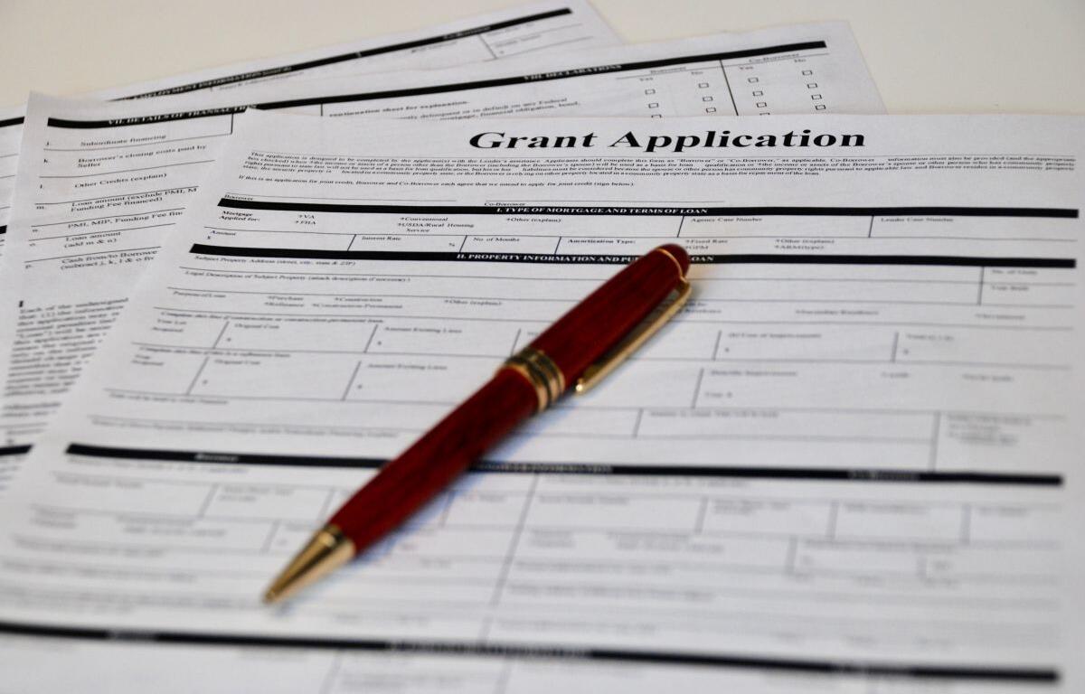 Grant application form with a red fountain pen resting on top on a white table.