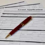 Grant application form with a red fountain pen resting on top on a white table.
