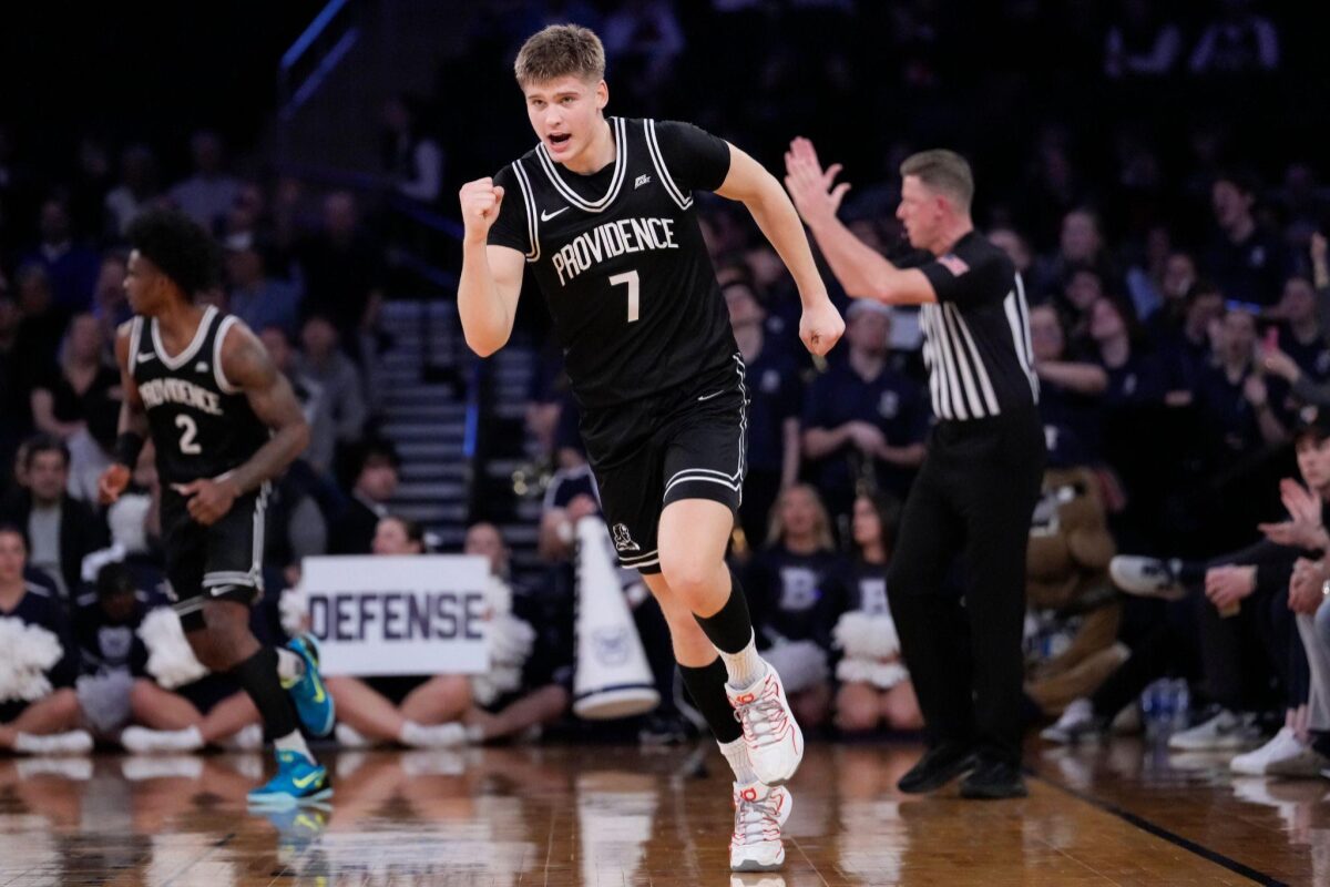 Providence basketball player in black jersey (number 1) sprinting on the court during a game, with defender and referee in background.