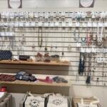 Jewelry display wall with hanging earrings, necklaces, and bracelets on a slat wall, plus a wooden counter with small accessories and bags beneath.