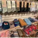 Display of colorful socks hanging on a rack above folded knit scarves in a shop.