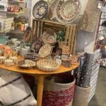 Round wooden table displays woven baskets, mugs, and bowls in a home decor shop.