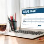 Laptop on a wooden desk showing an online survey form on screen, with star ratings and a text box for feedback