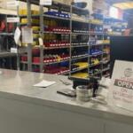 Checkout counter at a hardware store; organized shelves with red, yellow, and blue bins behind; sign reads 'We are open on Saturdays 8am–Noon'