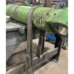 Green, worn metal beam on a metal stand in a workshop, with two frayed fabric straps hanging from the beam.